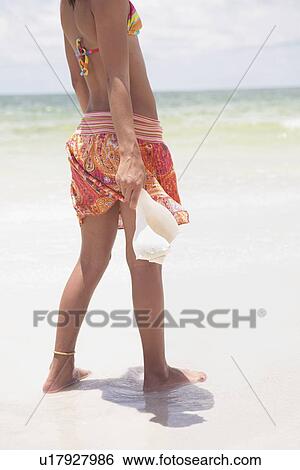 Girl standing in ocean holding shell View Large Photo Image Stock Photograph - Girl standing in ocean holding shell. Fotosearch