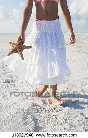 Stock Photo - Girl walking with starfish on beach. Fotosearch