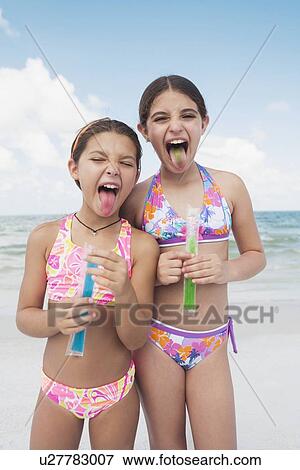 Stock Photo - Girls eating ice pops on beach. Fotosearch