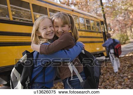 Stock Photography - Girls hugging in front of school bus. Fotosearch