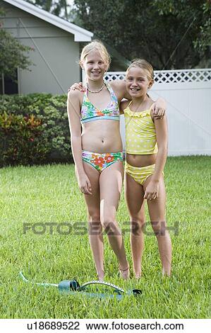 Stock Image - Girls playing with sprinkler in backyard. Fotosearch