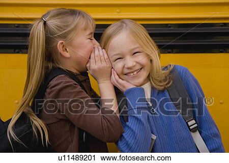 Stock Image - Girls telling secret in front of school bus. Fotosearch
