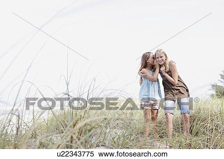 Girls telling secrets on grassy sand dune View Large Photo Image Stock Photography - Girls telling secrets on grassy sand dune. Fotosearch