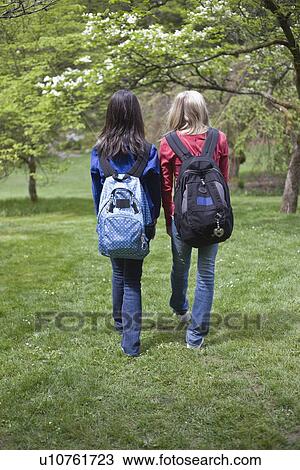Stock Image - Girls with backpacks walking in park. Fotosearch