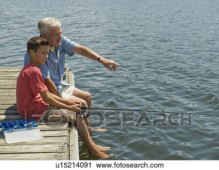 Stock Image - Grandfather and grandson fishing off dock. Fotosearch