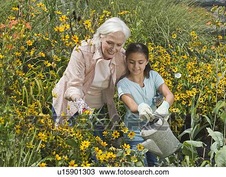 Stock Image - Grandmother and granddaughter watering plants. Fotosearch