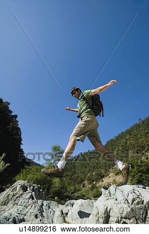 Stock Photograph - Hiker jumping across rocks. Fotosearch
