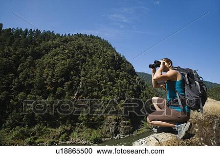 Stock Image - Hiker looking through binoculars on river overlook. Fotosearch