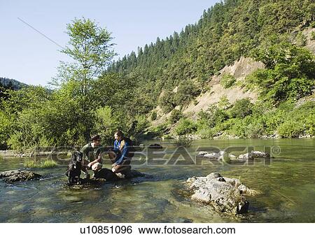 Hikers resting on rock in middle of river View Large Photo Image Stock Photograph - Hikers resting on rock in middle of river. Fotosearch