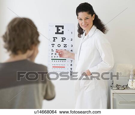 Picture - Hispanic female doctor pointing at eye chart for child. Fotosearch