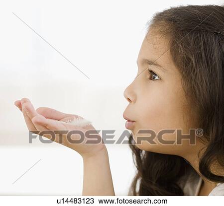 Stock Image - Hispanic girl blowing on feather in hand. Fotosearch