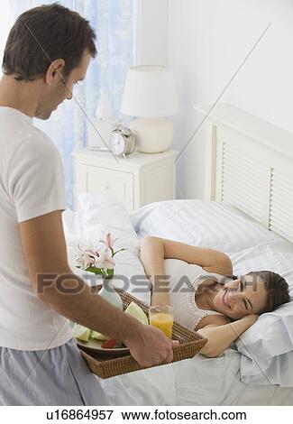 Stock Photo - Hispanic man bringing wife breakfast in bed. Fotosearch