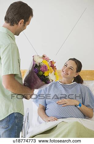 Stock Image - Hispanic man giving flowers to pregnant wife. Fotosearch