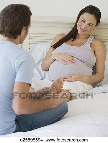 Picture - Hispanic man massaging pregnant wife’s foot. Fotosearch