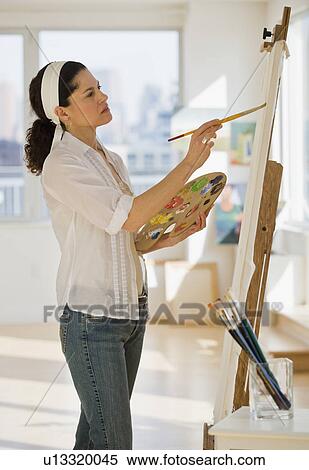 Stock Photography - Hispanic woman painting on easel. Fotosearch