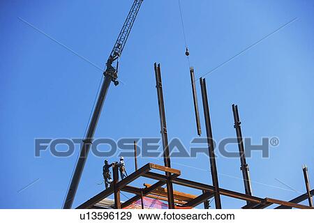 Stock Photo - Low angle view of construction workers on beam. Fotosearch