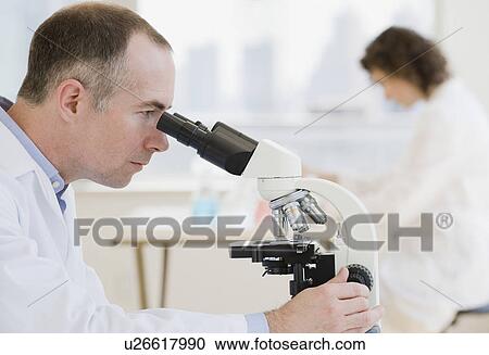 Stock Image - Male scientist looking into microscope. Fotosearch