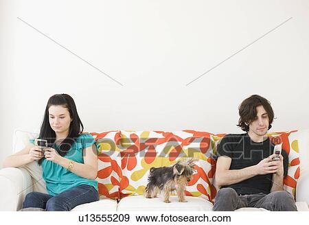 Stock Photo - Man and woman dialing cell phones on opposite ends of sofa. Fotosearch