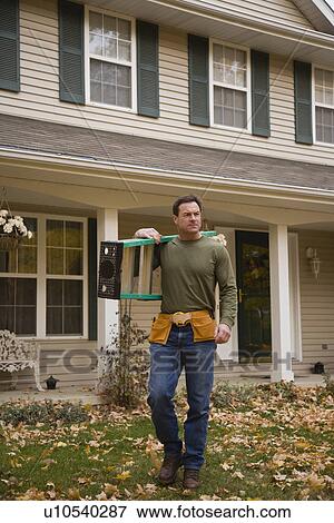 Stock Photo - Man carrying ladder next to house. Fotosearch