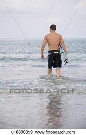 Man carrying surfboard into water View Large Photo Image Stock Photo - Man carrying surfboard into water. Fotosearch