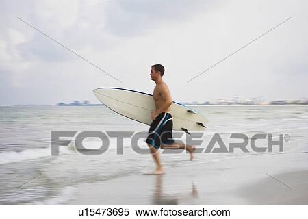 Man carrying surfboard into water View Large Photo Image Stock Photography - Man carrying surfboard into water. Fotosearch