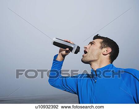 Stock Image - Man drinking from water bottle on foggy beach. Fotosearch