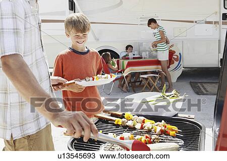 Stock Image - Man grilling dinner for family on beach. Fotosearch