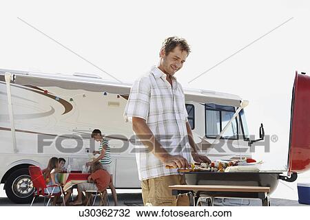 Stock Image - Man grilling dinner for family on beach. Fotosearch