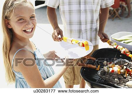 Stock Photo - Man grilling dinner for family on beach. Fotosearch