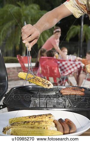 Man grilling hotdogs and corn in backyard View Large Photo Image Stock Image - Man grilling hotdogs and corn in backyard. Fotosearch