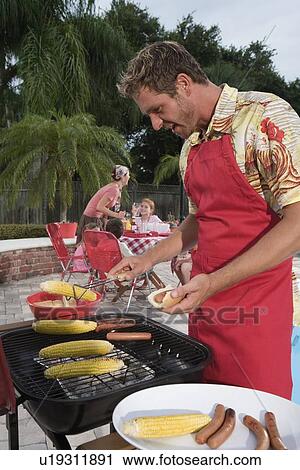 Man grilling hotdogs and corn in backyard View Large Photo Image Stock Image - Man grilling hotdogs and corn in backyard. Fotosearch