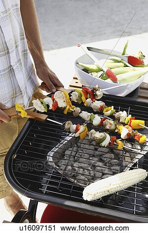 Stock Image - Man grilling shish kebabs and corn. Fotosearch