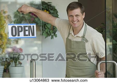 Stock Image - Man hanging open sign in flower shop window. Fotosearch