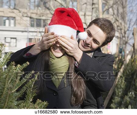 Stock Image - Man holding hands over girlfriend’s eyes. Fotosearch