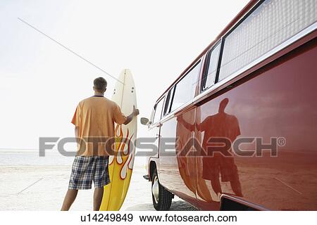 Man holding surfboard next to van on beach View Large Photo Image Stock Photo - Man holding surfboard next to van on beach. Fotosearch
