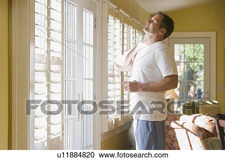 Stock Image - Man in pajamas looking out window. Fotosearch