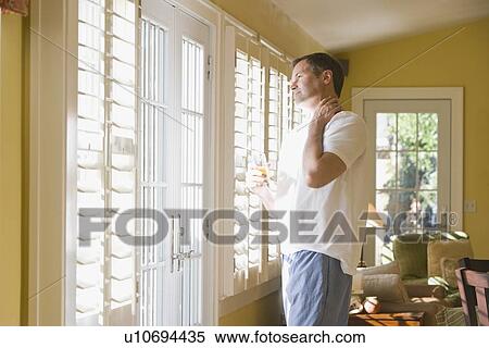 Stock Photography - Man in pajamas looking out window. Fotosearch