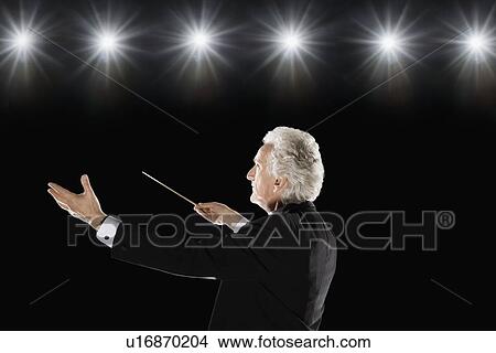 Picture - Man in tuxedo conducting under lights. Fotosearch