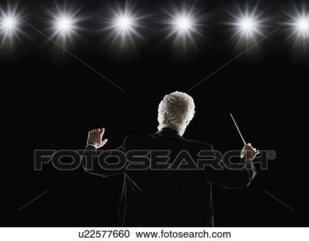 Stock Image - Man in tuxedo conducting under lights. Fotosearch