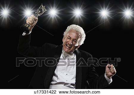 Stock Image - Man in tuxedo holding trophy. Fotosearch