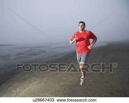 Stock Image - Man jogging on foggy beach. Fotosearch