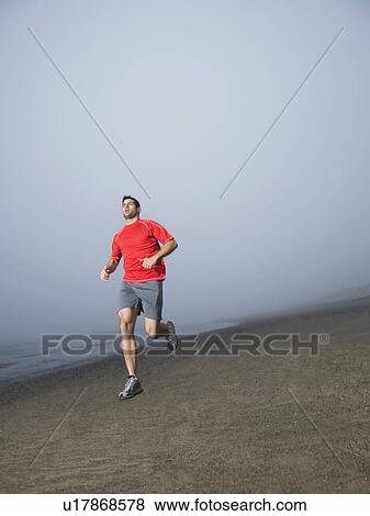 Stock Photo - Man jogging on foggy beach. Fotosearch