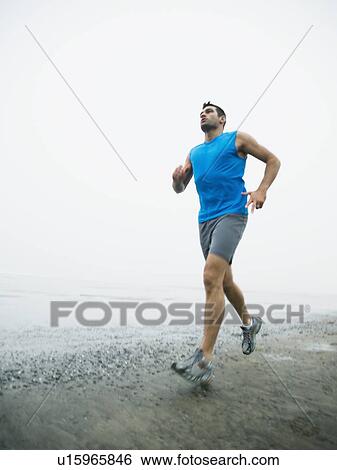 Stock Photograph - Man jogging on foggy beach. Fotosearch