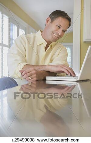 Man looking at laptop in kitchen View Large Photo Image Stock Photo - Man looking at laptop in kitchen. Fotosearch