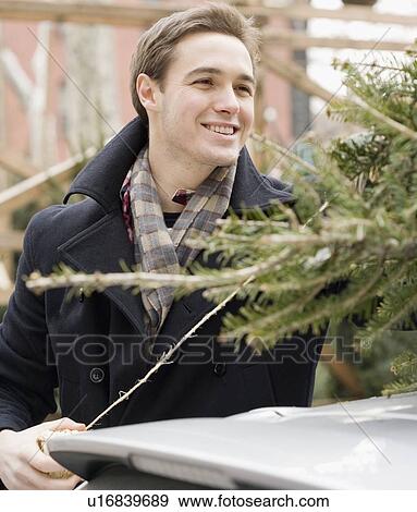 Stock Photo - Man next to Christmas tree on car. Fotosearch