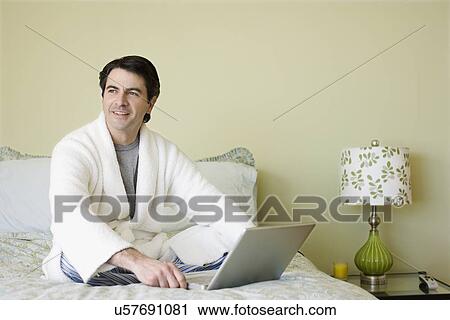Stock Image - Man next to laptop on bed. Fotosearch
