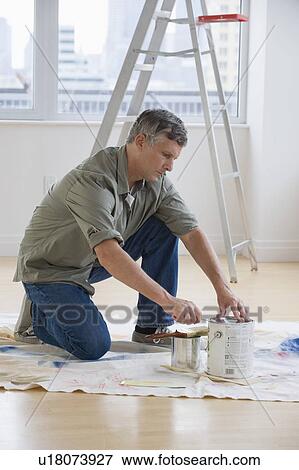 Stock Photo - Man opening paint cans on drop cloth. Fotosearch