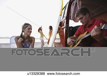 Stock Photo - Man playing guitar in van on beach. Fotosearch