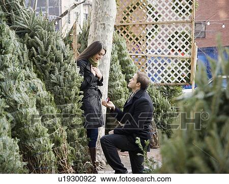Stock Image - Man proposing to girlfriend on Christmas tree lot. Fotosearch