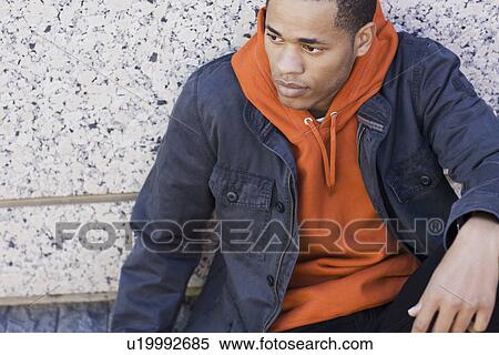 Stock Photography - Man sitting against wall looking worried. Fotosearch